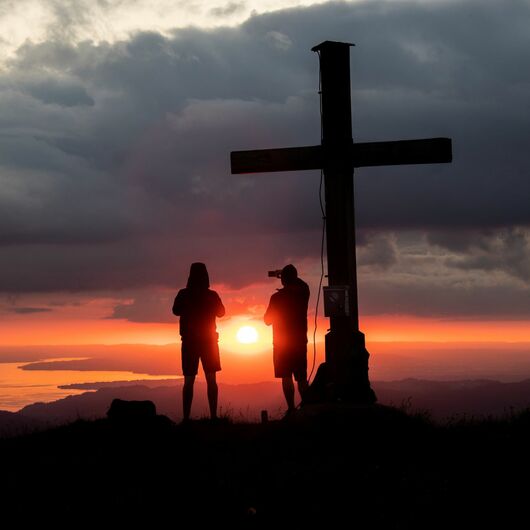 Zwei Menschen beim Sonnenuntergang auf der Bergspitze beim Bergkreuz